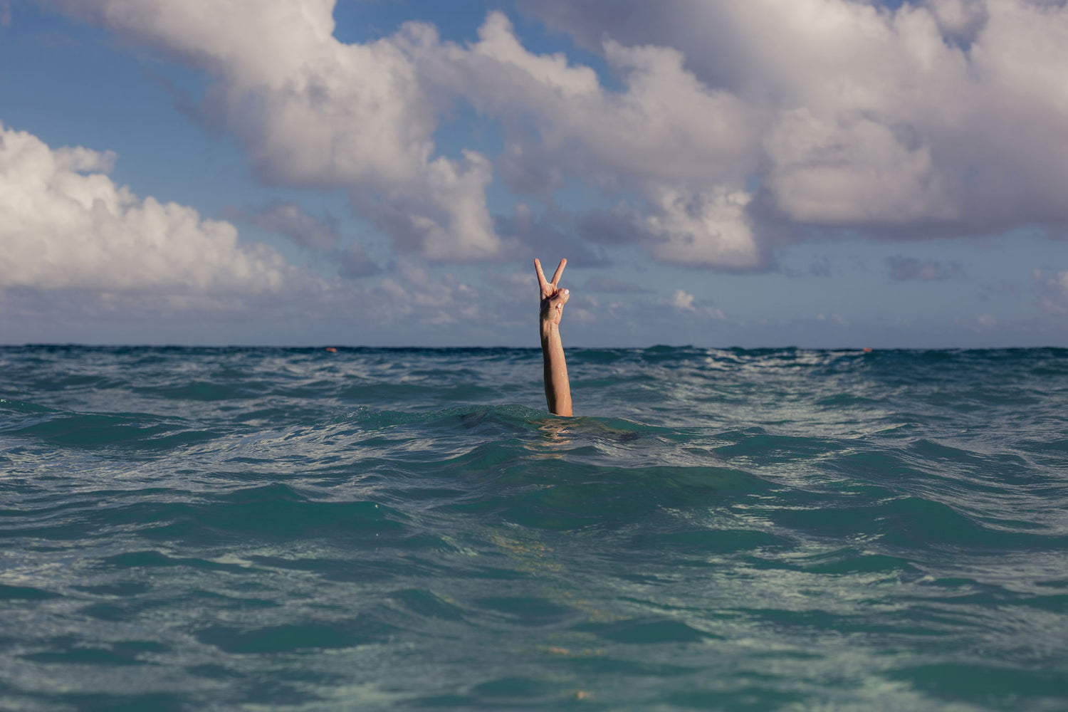 Person on enjoying tropical vacation and giving peace sign while under water 